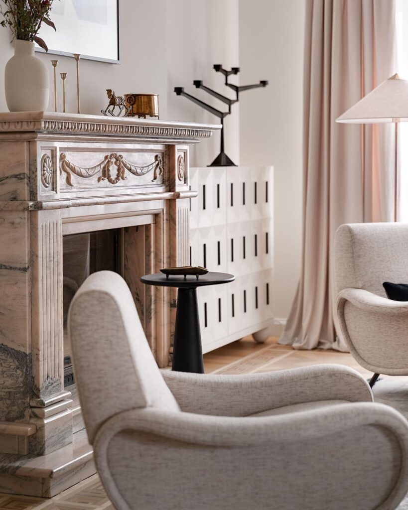 Elegant Fireplace Mantel With Decorative Carvings And Lighting Fixtures In A Cozy Living Room Setting Designed By Sivak+Partners.