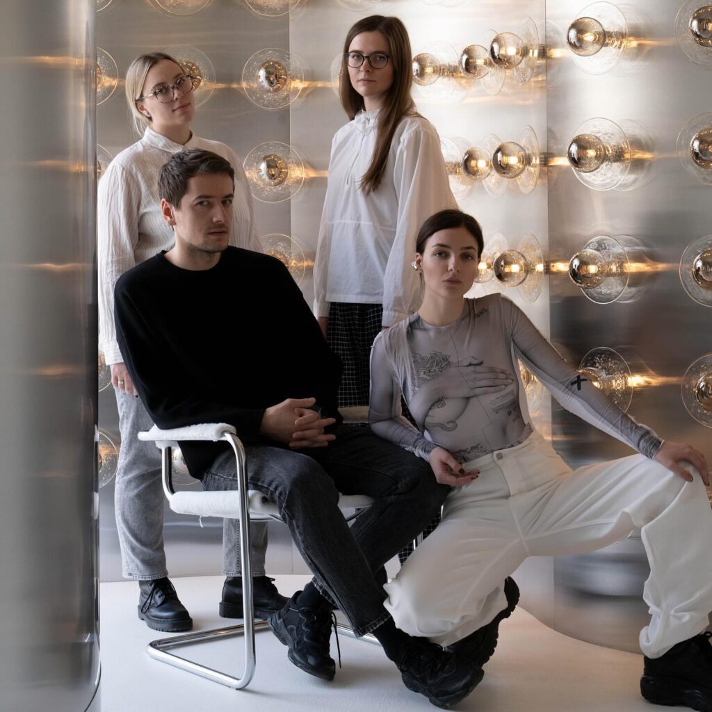 A Group Of Young People Posing In A Minimalist Interior Design Setting With Spherical Glass Lighting Fixtures On The Wall