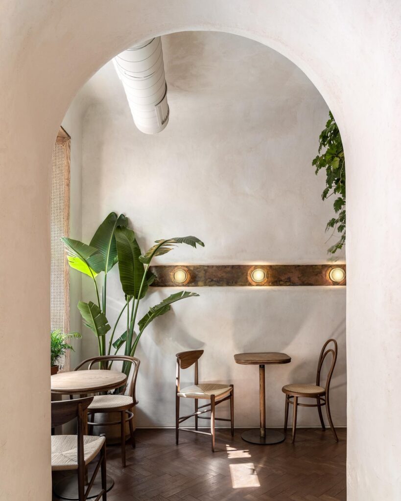 An Intimate Interior Design Space With Arched Entryway, Potted Plants, and Wooden Furniture Pieces Designed by Sivak+Partners.