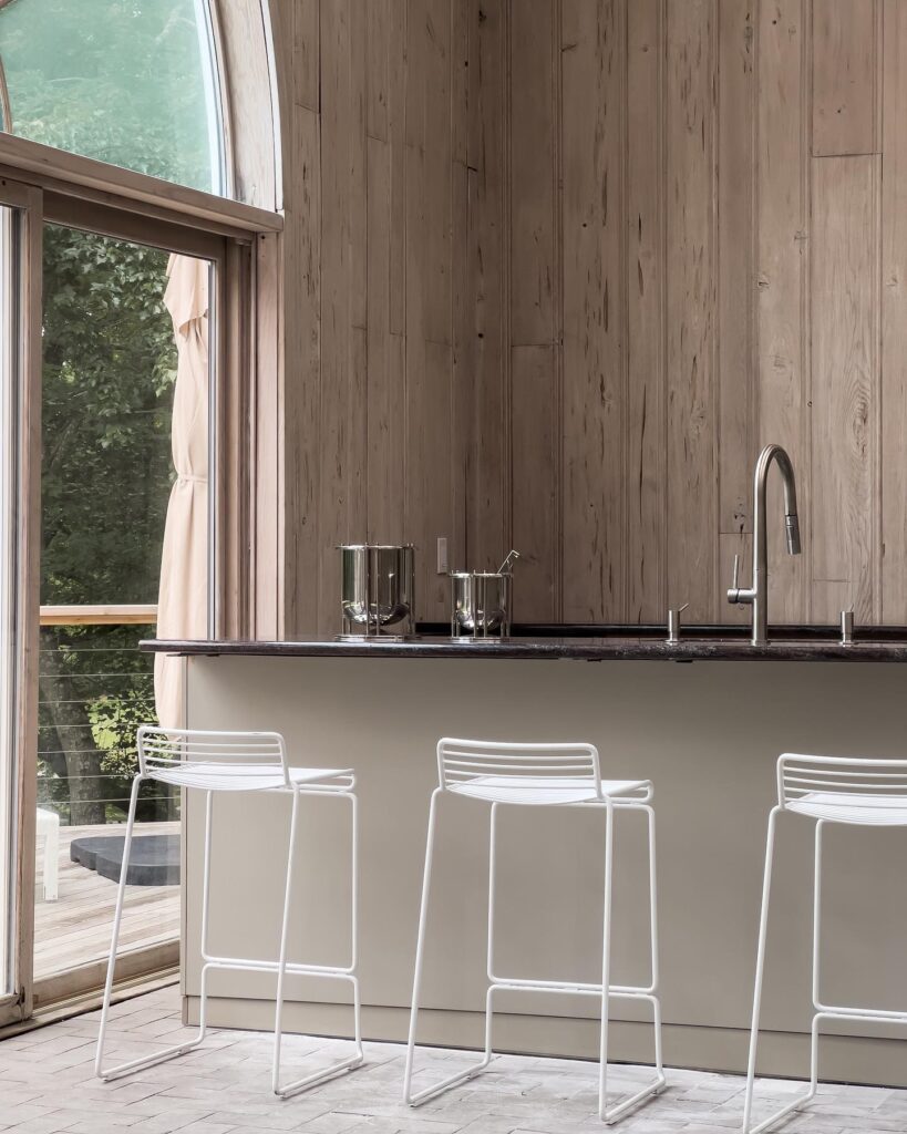 A modern kitchen interior with wooden walls and sleek white bar stools.