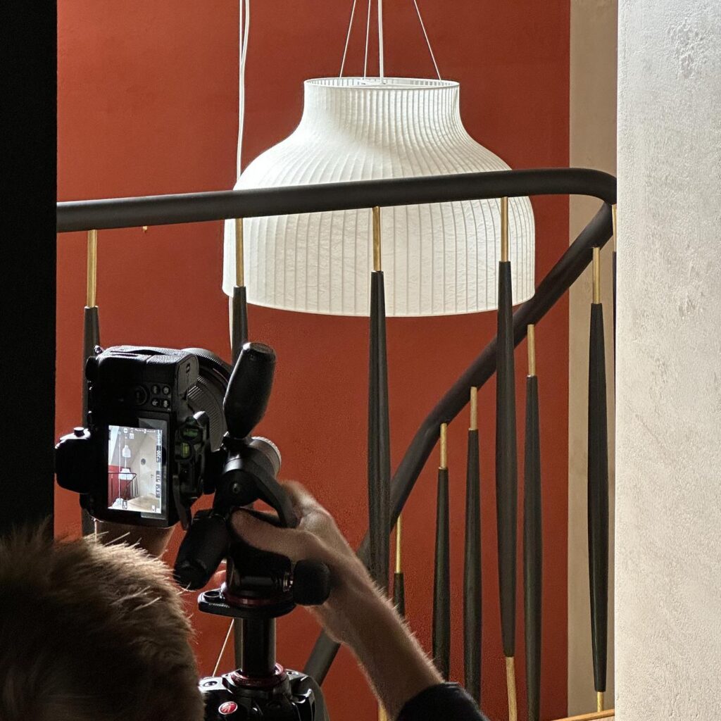 A Pendant Light Fixture Hangs Above a Camera Tripod in a Studio Setting with a Red Wall