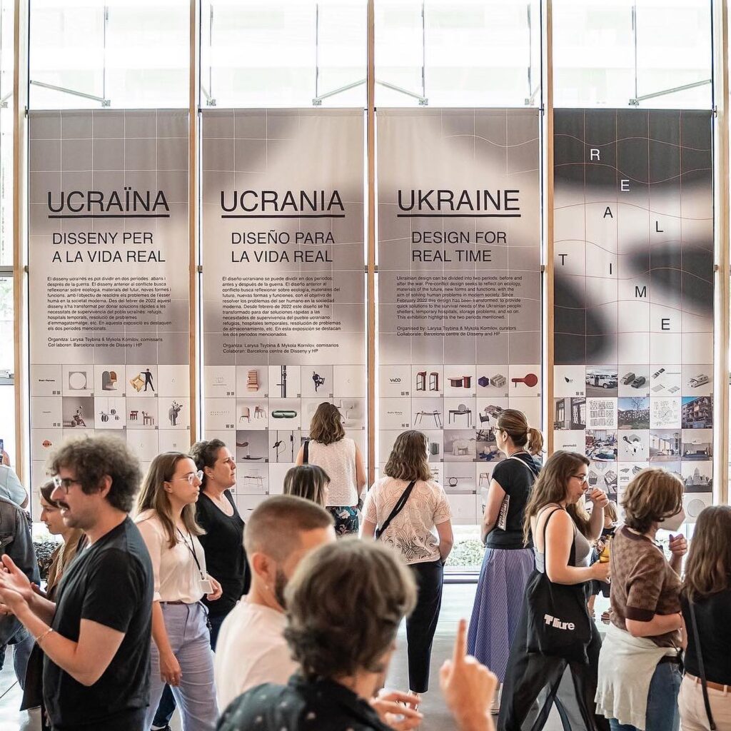 The Alt Text for the image is: A Group Of People Gathered In Front Of Large Display Panels Showcasing The Work Of Ucrania, A Design Studio Focused On Interior And Exterior Design
